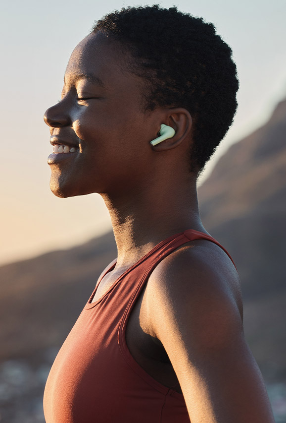 Photo of a woman in workout clothes wearing headphones smiling outside